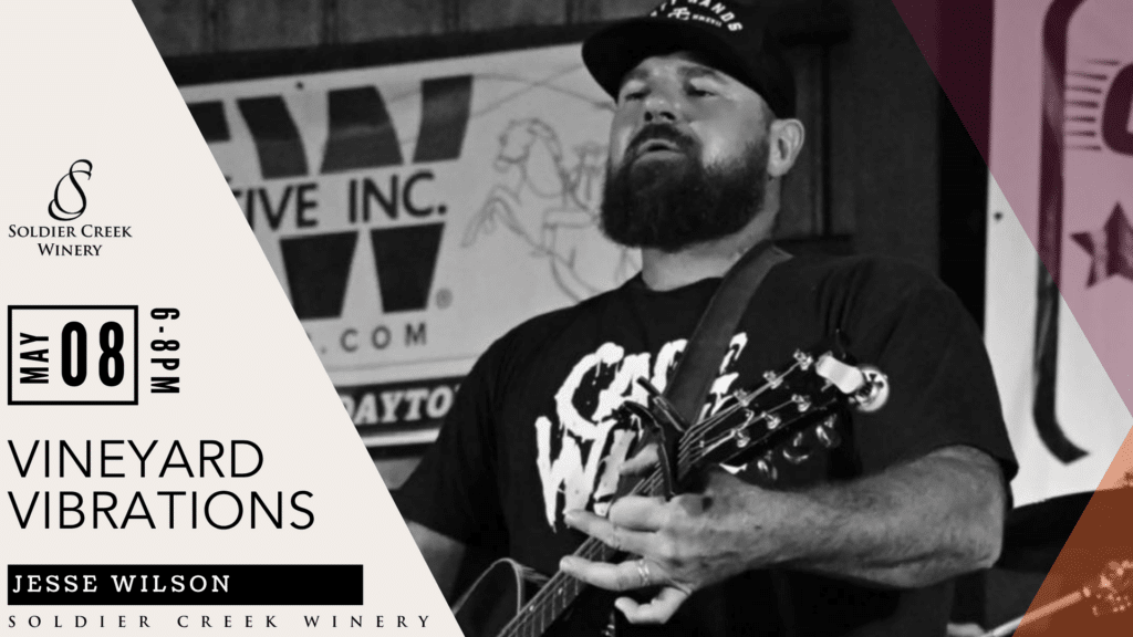 Vineyard Vibrations live music event at Soldier Creek Winery featuring Jesse Wilson on May 8, 6–8pm. Black-and-white photo shows a bearded man in a cap playing guitar and singing outdoors.